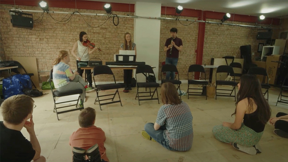 A group of young adults sitting on the floor with a few adults playing musical instruments.